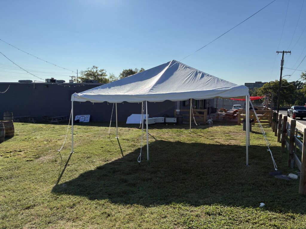 white pop up canopy tent set up on a grassy yard with string lights and a wooden fence on the right side