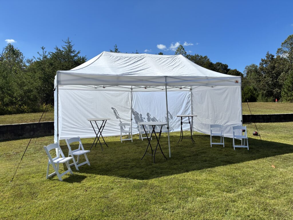 white event canopy set up on a grassy field with folding tables and chairs outdoors